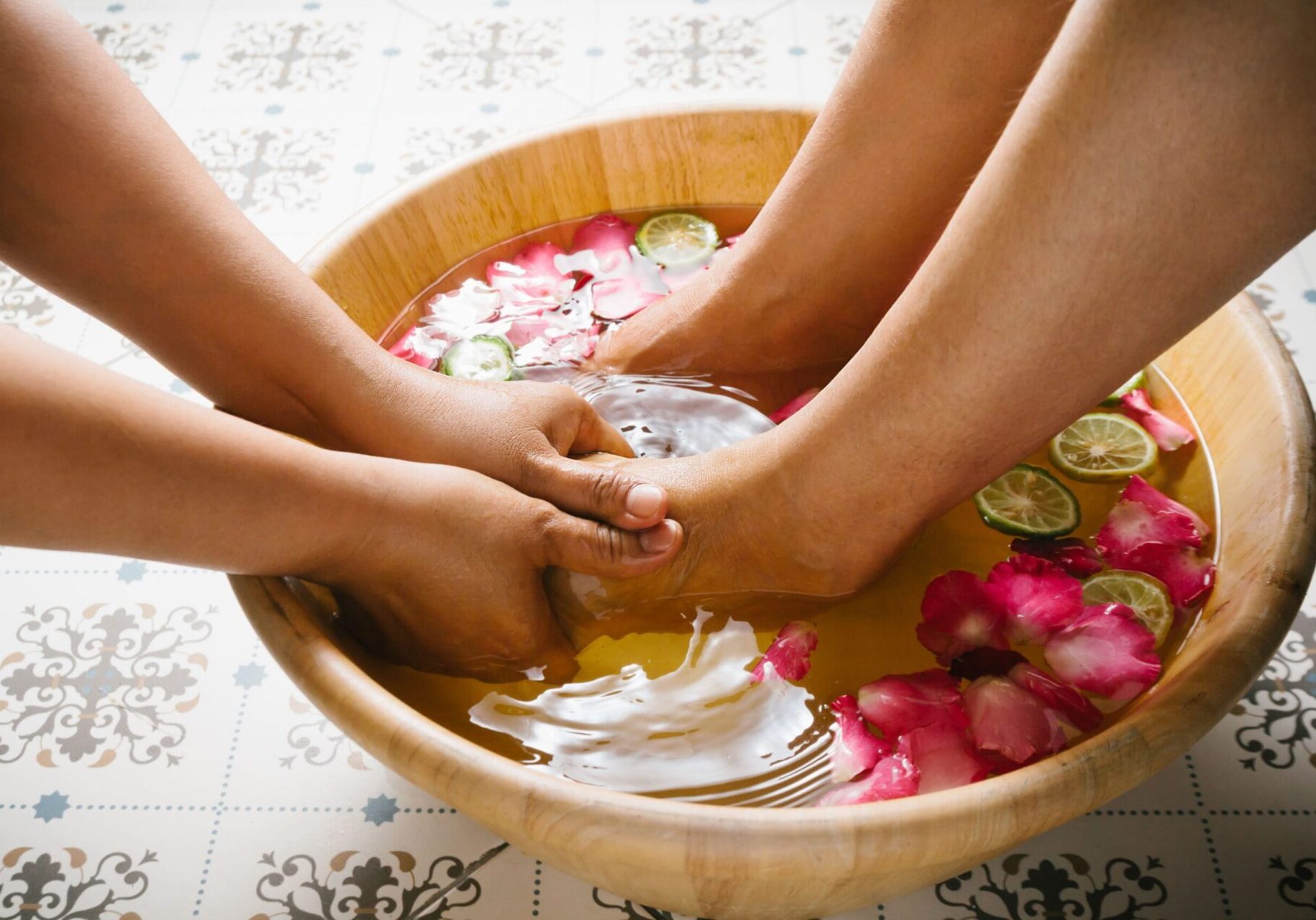 Mains massant des pieds dans un bols d'eau aux pétales de rose-forfait.